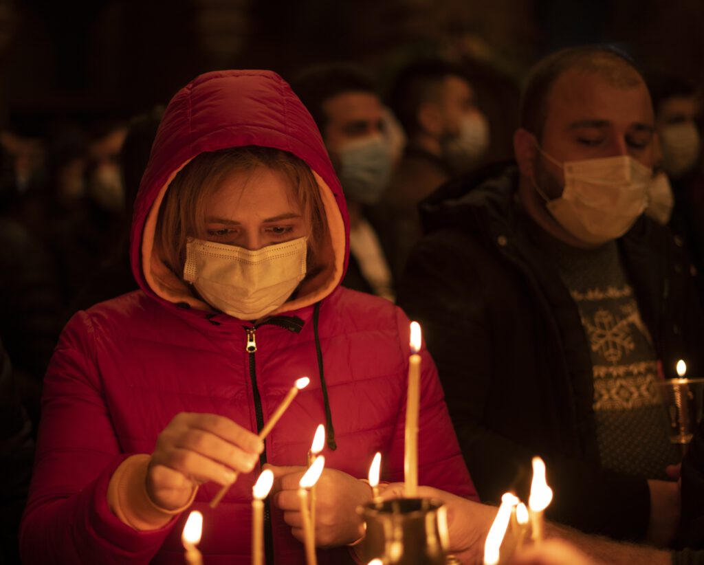 Eine Frau mit Mundschutz zündet eine Kerze an